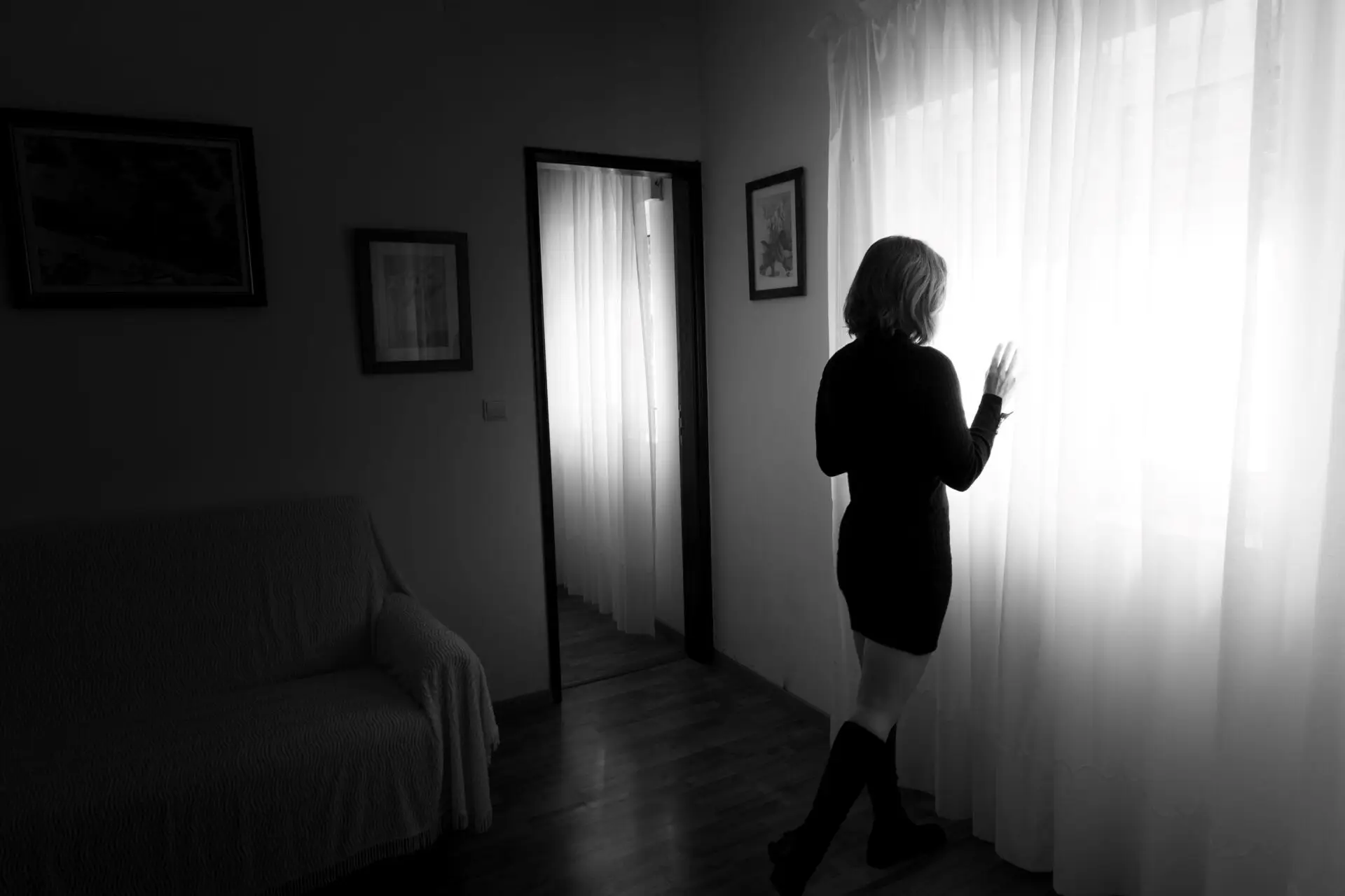 Frau steht allein am Fenster in einer Wohnung